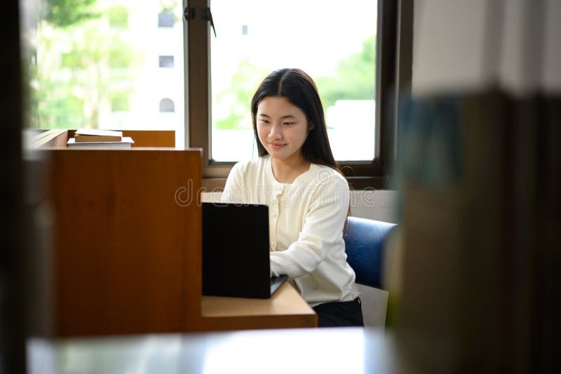 Teenage girl education concept. Her using laptop in library stock photography