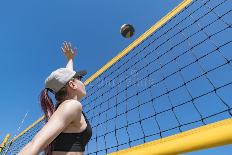 Teenage girl playing beach volleyball. Beach volleyball championship. The woman reaches for the ball. throwing a yellow volleyball over the net. Victory point. Outdoor sports games. Teenage girl playing beach volleyball. Beach volleyball championship. The woman reaches for the ball. throwing a yellow volleyball over the net. Victory point. Outdoor sports games.