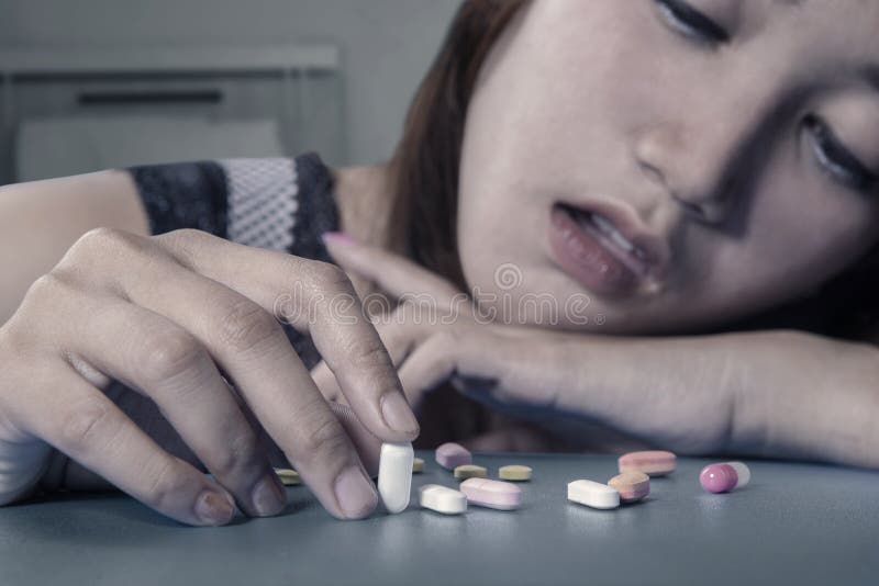 Depressed female drug addict holding pills on the table, shot at home. Depressed female drug addict holding pills on the table, shot at home