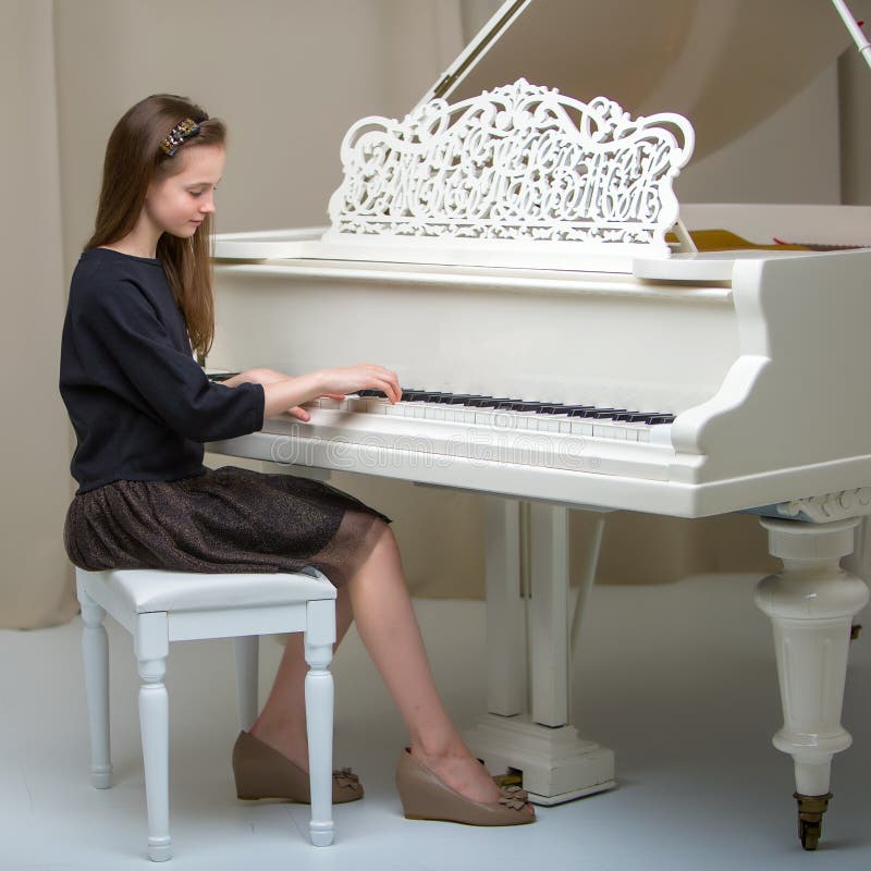 A teenage girl is playing on a white grand piano.