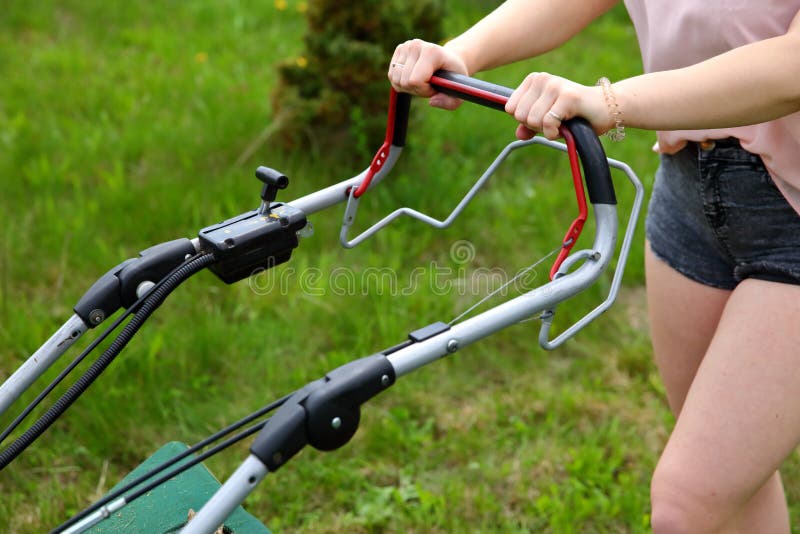 Teenage girl pruning green high grass with the help of an petrol lawn mower. royalty free stock photography Teenage girl pruning green high grass with the help of an petrol lawn mower. royalty free stock photography