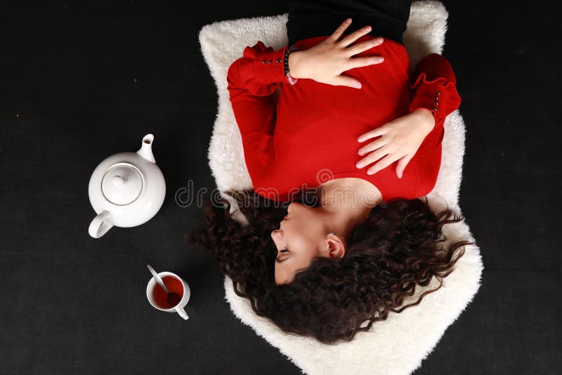 Teenage girl in red blouse and black pantyhose  lying aside tea cup and teapot. Black background. Tea party concept. Teenage girl in red blouse and black pantyhose  lying aside tea cup and teapot. Black background. Tea party concept.