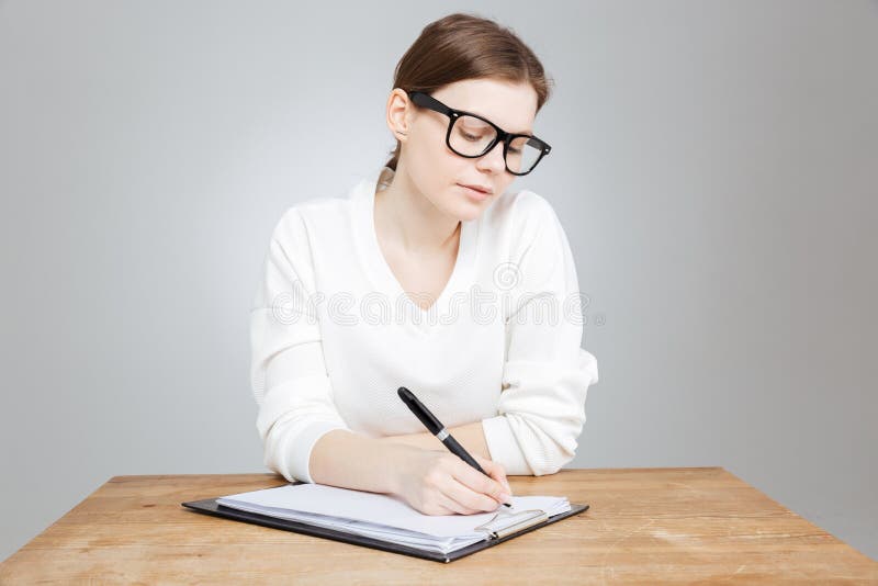 Teenage girl sitting and writing on clipboard.