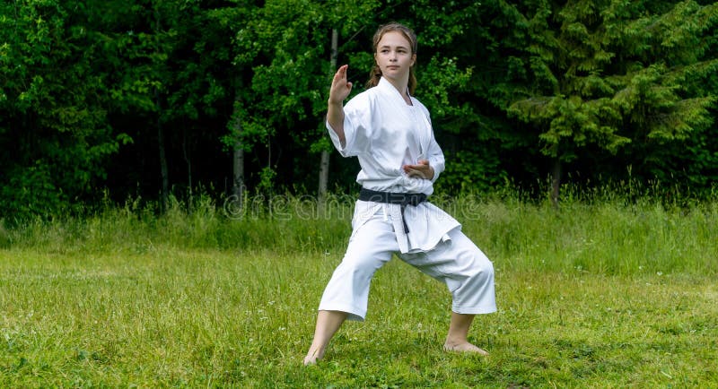 Teenage girl training karate kata outdoors, performs soto uke or outside block in kakutsu dachi stand