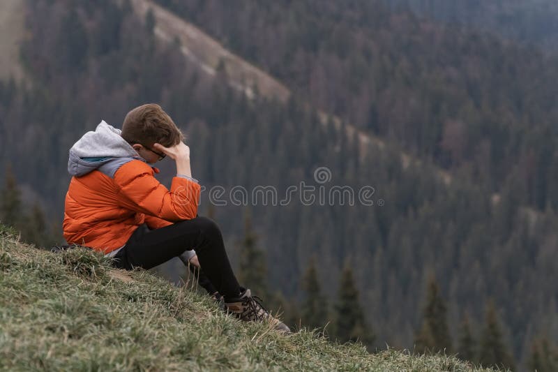 Teenage guy sits on hillside and thinks about something. Weekend in nature. Hiking and travelling with children