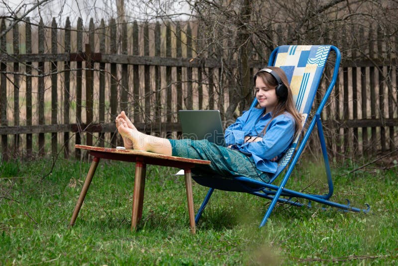 Teen girl takes part in a school online webinar sitting outdoors in springtime