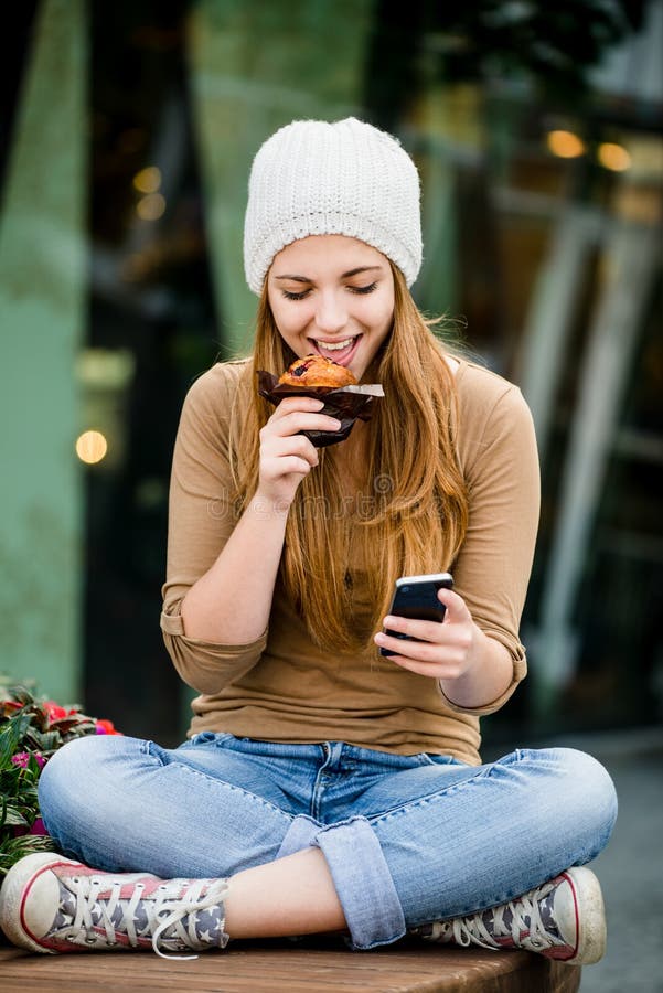 Teenager eating muffin looking in phone stock photography Teenager eating muffin looking in phone stock photography