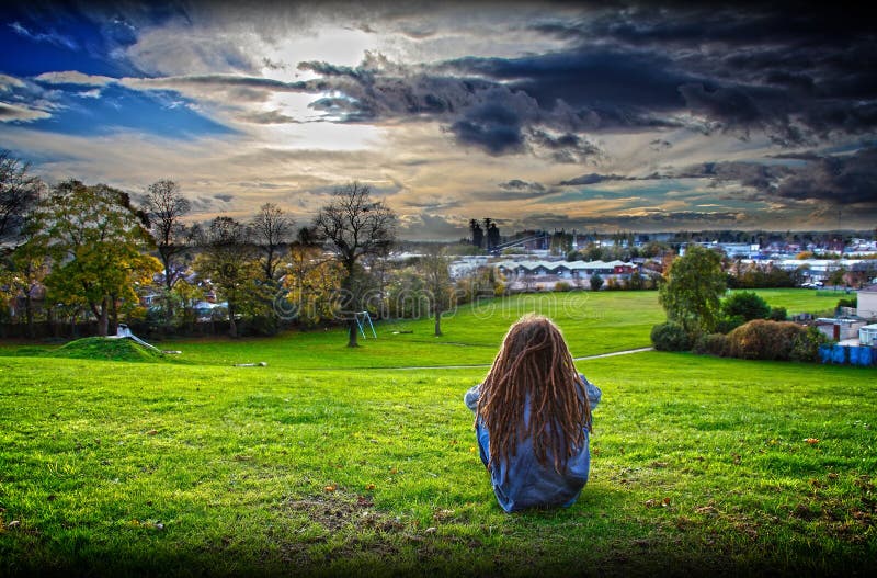 Grungy adolescente con i dreadlocks, seduta su di una collina a contemplare la vita in affidamento.