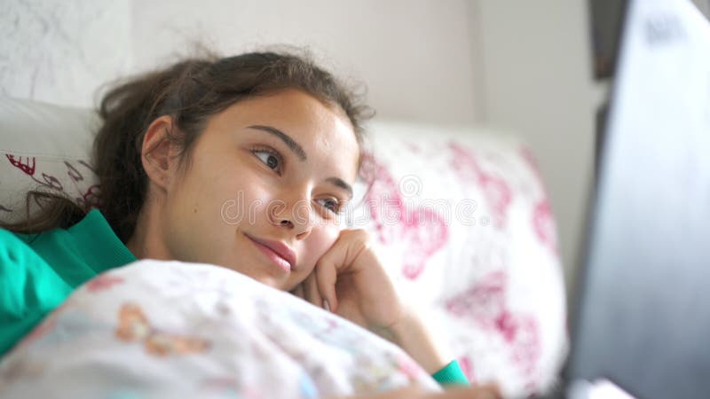 Teenager girl chats with friends via laptop lying in bed