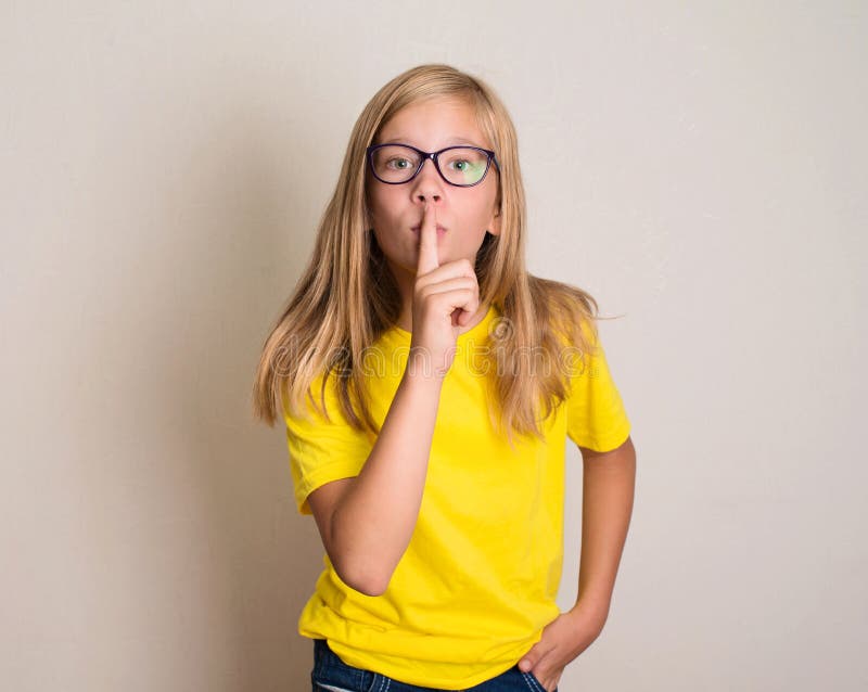 Teenager girl in eyeglasses putting finger up to lips and ask si