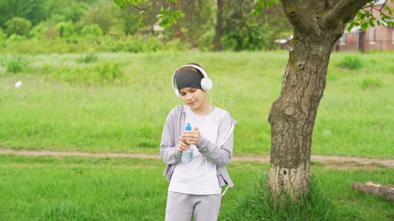 Teenager girl with headphones drinking water after jogging in the park.