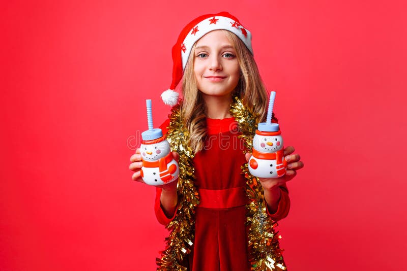 Teenager girl in Santa hat and tinsel on the neck, holds 2 bottles of juice Christmas in the shape of a snowman on a red stock photo Teenager girl in Santa hat and tinsel on the neck, holds 2 bottles of juice Christmas in the shape of a snowman on a red stock photo