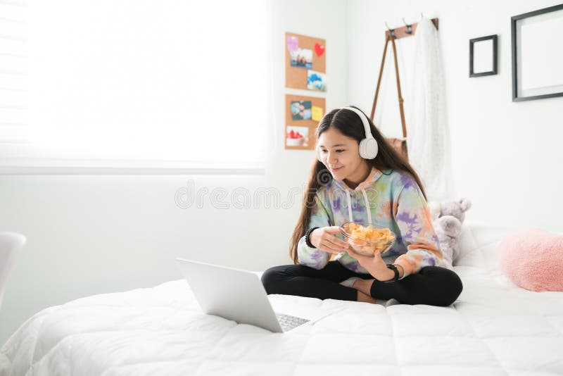 Teenager girl sitting in bed and enjoying a movie with chips