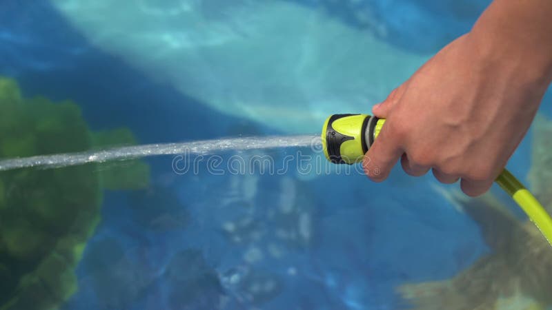 Teenager hand filling Inflatable pool with water from hose in garden in england uk