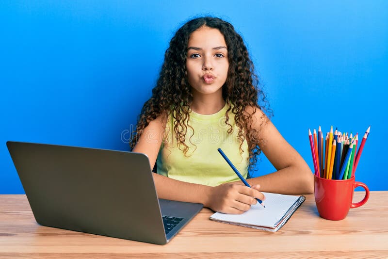 Teenager hispanic girl sitting on the table studying for school looking at the camera blowing a kiss being lovely and sexy. love expression