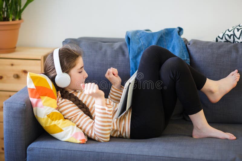 Teenager mit Kopfhörer auf liegt auf Couch und hört Musik. Mädchen mit Tablette lizenzfreie stockbilder