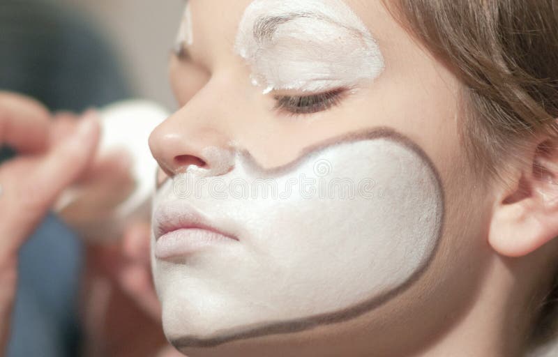 Closeup of teenager applying decorative white paint to face. Closeup of teenager applying decorative white paint to face.