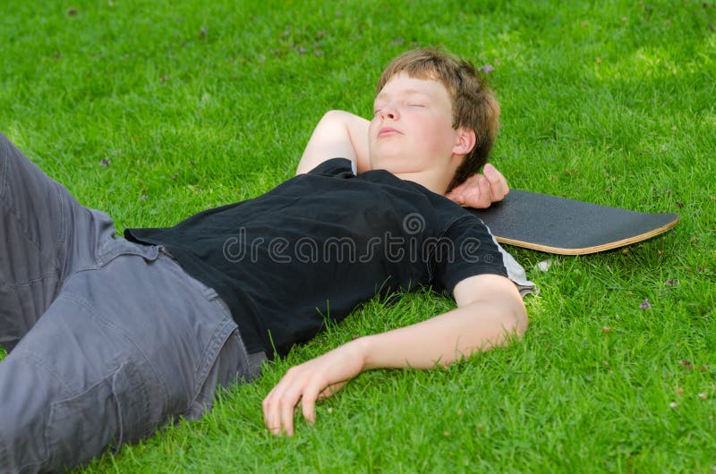 Teenager with skate resting or sleeps on the grass after active skateboarding. Teenager with skate resting or sleeps on the grass after active skateboarding