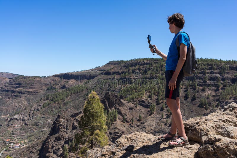 A teenager uses a three-axis image stabilizer to film a natural mountain landscape on a smartphone camera. stock photography