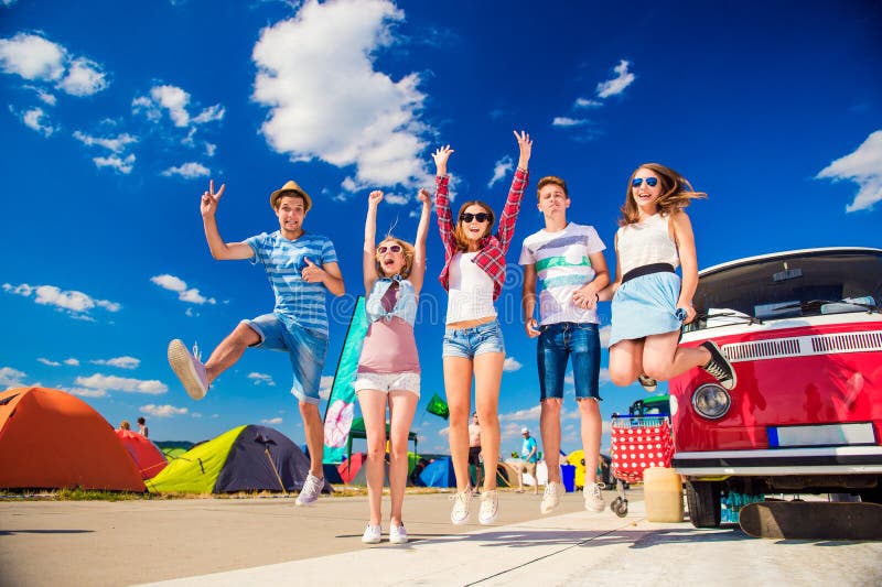 Teenagers at summer festival jumping by vintage red campervan