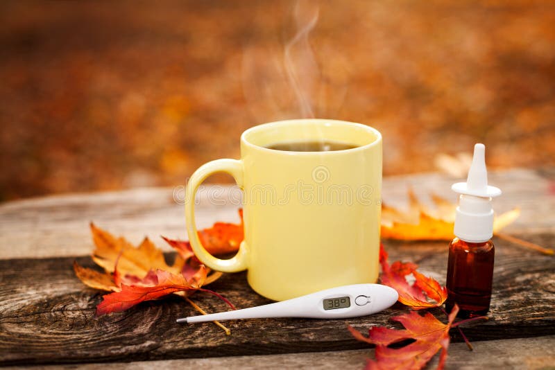 Tea cup with thermometer, autumn leaves and nose drops on wooden surface, flu season in autumn. Tea cup with thermometer, autumn leaves and nose drops on wooden surface, flu season in autumn