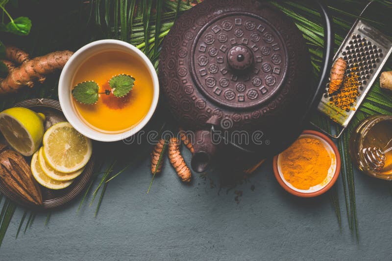Teapot and healthy turmeric spice tea with lemon, ginger and honey on dark background , top view. Immune boosting remedy , detox and dieting concept. Teapot and healthy turmeric spice tea with lemon, ginger and honey on dark background , top view. Immune boosting remedy , detox and dieting concept