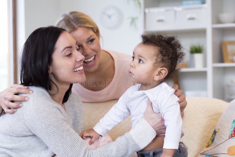 Female couple sitting in their home, playing with their baby son. Female couple sitting in their home, playing with their baby son.