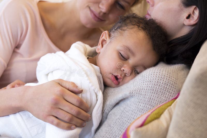 Same sex female couple lying down with their baby son. Same sex female couple lying down with their baby son