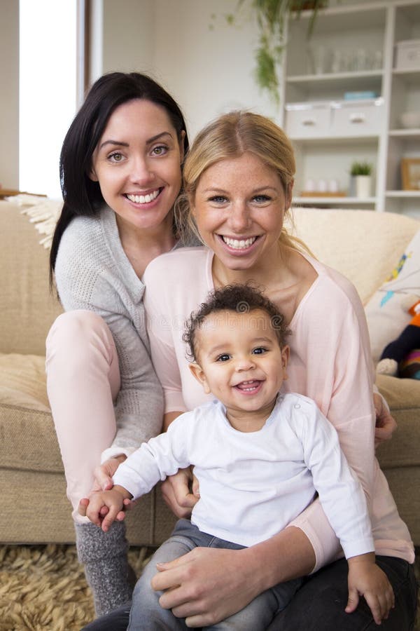 Female couple sit together with their son in their home and all smile for the camera. Female couple sit together with their son in their home and all smile for the camera