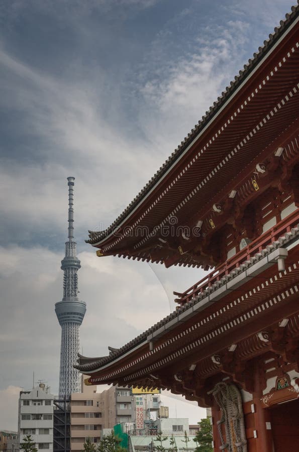 Tokyo, Japan - September 26, 2016: Part of vermilion roof of Hozomon Gate at Senso-ji Buddhist Temple with tall Skytree tower in the distance under blue cloudy sky. Tokyo, Japan - September 26, 2016: Part of vermilion roof of Hozomon Gate at Senso-ji Buddhist Temple with tall Skytree tower in the distance under blue cloudy sky.