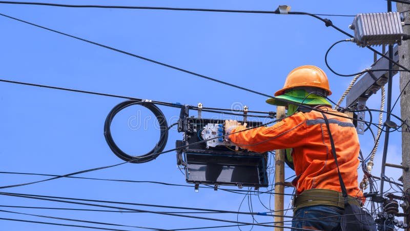 Rear view of technician on wooden ladder is working to install fiber optic and splitter box on electric pole against blue sky background. Rear view of technician on wooden ladder is working to install fiber optic and splitter box on electric pole against blue sky background