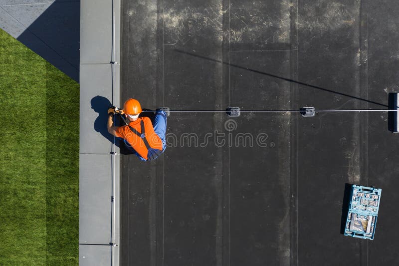 Caucasian Technician Wearing Orange Uniform and Hard Hat Installing Lightning Protection System Rod on Top of Commercial Building. Protect Structure From Elements. Caucasian Technician Wearing Orange Uniform and Hard Hat Installing Lightning Protection System Rod on Top of Commercial Building. Protect Structure From Elements