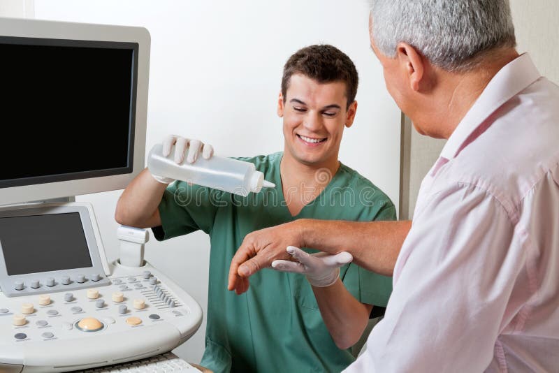 Young male radiologic technician smiling while putting gel to male patient's hand. Young male radiologic technician smiling while putting gel to male patient's hand