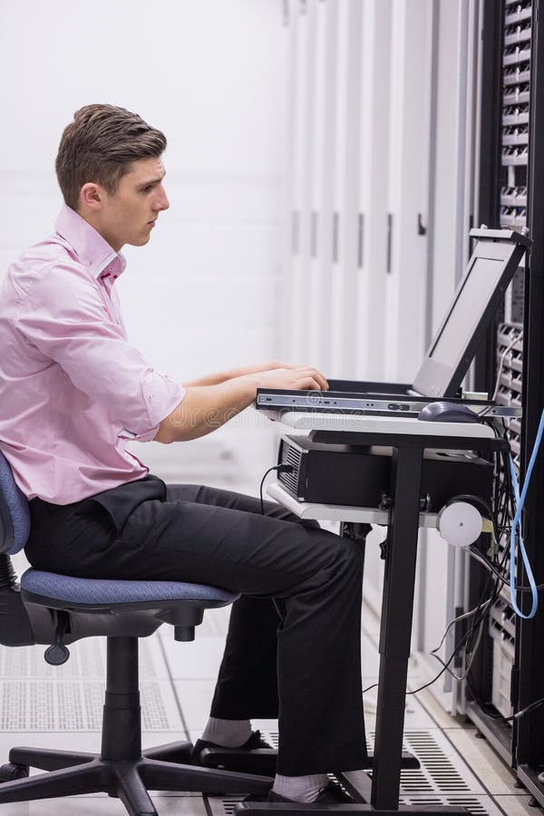 Teknikersammanträde på svängtappstol som använder bärbara datorn för att diagnostisera serveror arkivbilder Teknikersammanträde på svängtappstol som använder bärbara datorn för att diagnostisera serveror arkivbilder