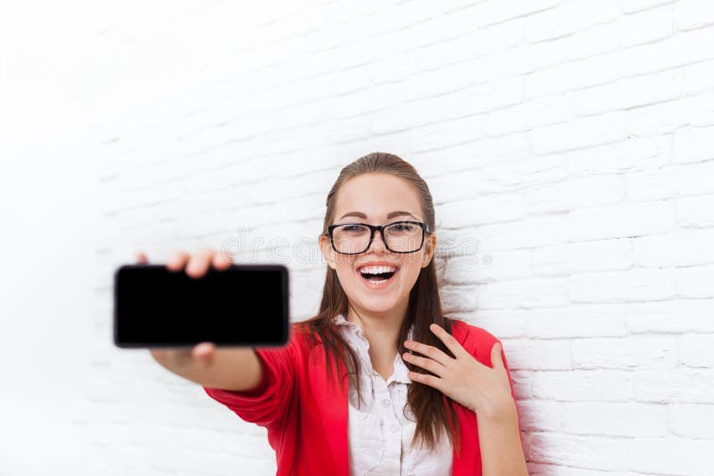 Tela esperta do telefone da pilha da mostra da mulher de negócios com sorriso feliz dos vidros vermelhos vazios do revestimento d fotografia de stock royalty free Tela esperta do telefone da pilha da mostra da mulher de negócios com sorriso feliz dos vidros vermelhos vazios do revestimento d fotografia de stock royalty free
