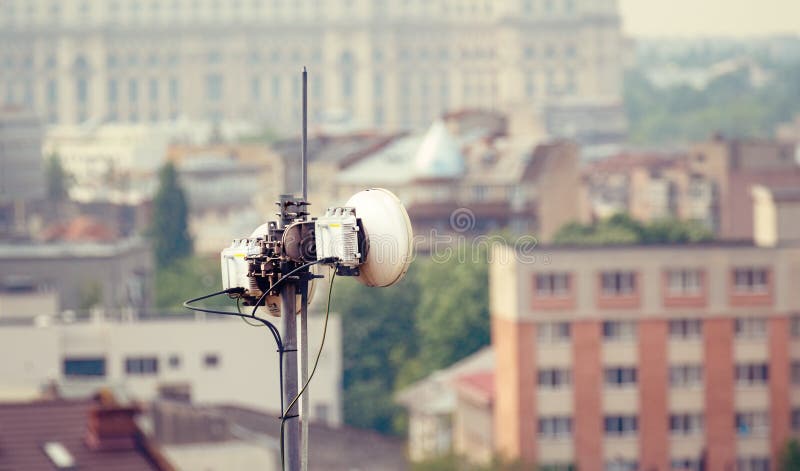 Telecommunication microwave antenna dish on a building rooftop with the city in background stock photo Telecommunication microwave antenna dish on a building rooftop with the city in background stock photo