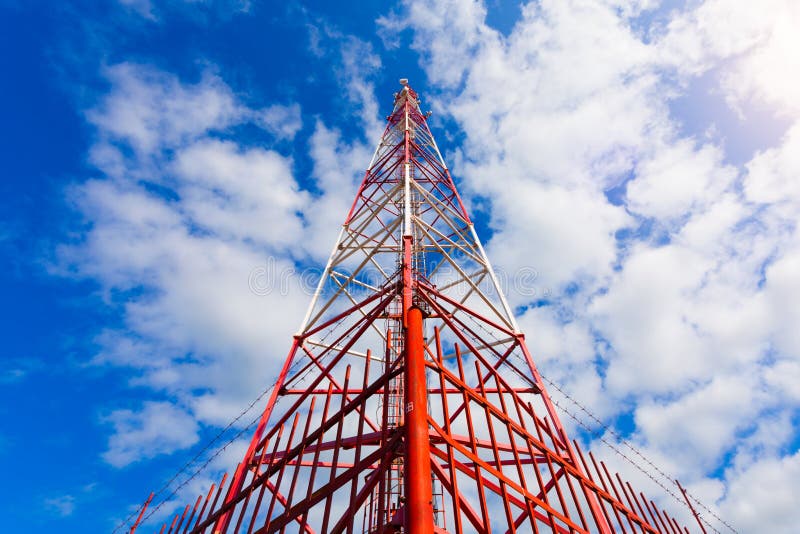 Inside view of telecommunication tower with panel antennas and radio antennas and satellite dishes for mobile communications 2G, 3G, 4G, 5G with red fence around tower against blue sky with clouds