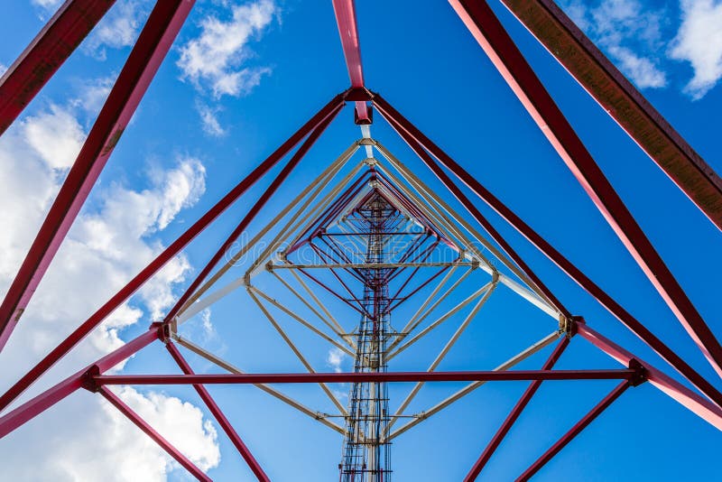 Inside view of telecommunication tower with panel antennas and radio antennas and satellite dishes for mobile communications 2G, 3G, 4G, 5G with red fence around tower against blue sky with clouds