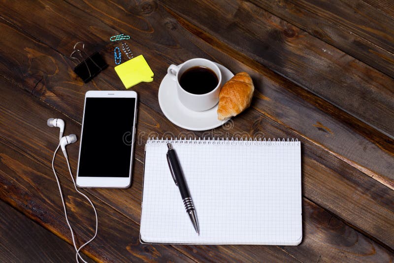 Telefone celular branco no fundo de madeira de madeira com os dispositivos dos fones de ouvido, da xícara de café, do croissant e fotos de stock Telefone celular branco no fundo de madeira de madeira com os dispositivos dos fones de ouvido, da xícara de café, do croissant e fotos de stock