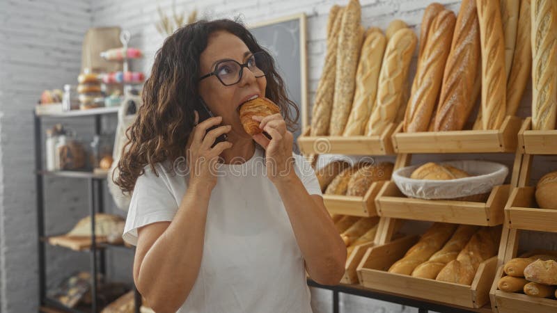 Telefonische Frau beim Backen in einer Bäckerei mit verschiedenen Brotlaiben im Hintergrund lizenzfreies stockbild