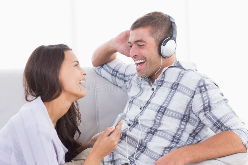 Telefono cellulare della tenuta della donna mentre musica d'ascolto dell'uomo fotografia stock libera da diritti Telefono cellulare della tenuta della donna mentre musica d'ascolto dell'uomo fotografia stock libera da diritti