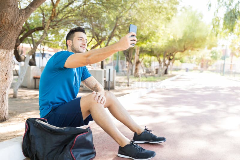 Telefono cellulare di Taking Selfie Using dell'atleta mentre sedendosi nel parco fotografia stock Telefono cellulare di Taking Selfie Using dell'atleta mentre sedendosi nel parco fotografia stock