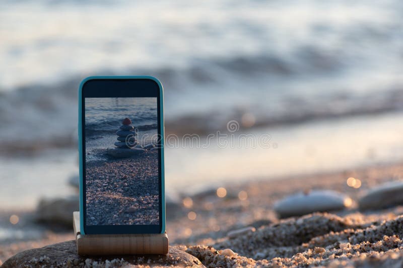 Telefono cellulare sulla piramide di immagini di una spiaggia in mare sullo sfondo marino dello schermo di smartphone. foto di via fotografia stock