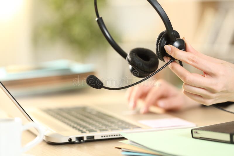 Telemarketer holding headset working on laptop