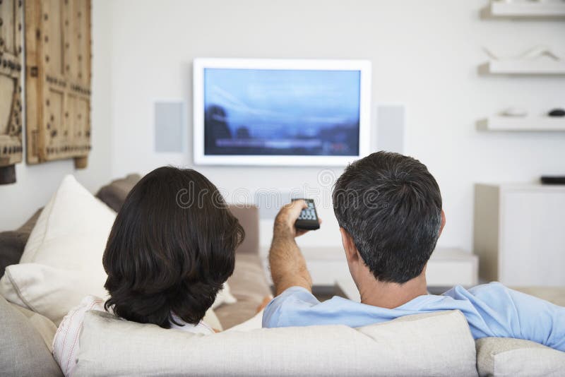 Televisão de observação dos pares na sala de visitas imagem de stock Televisão de observação dos pares na sala de visitas imagem de stock