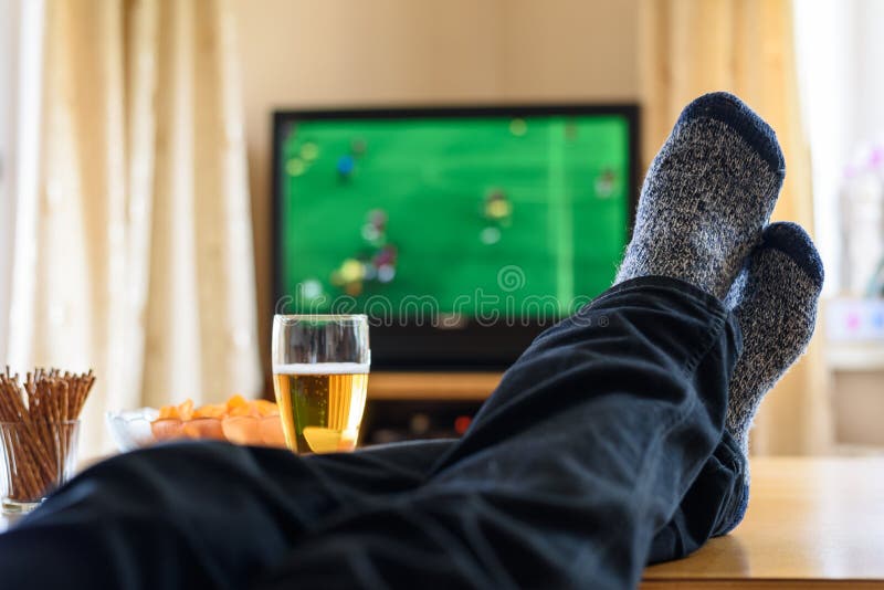 Televisão, tevê que olha (fósforo de futebol) com pés na tabela e imagem de stock Televisão, tevê que olha (fósforo de futebol) com pés na tabela e imagem de stock