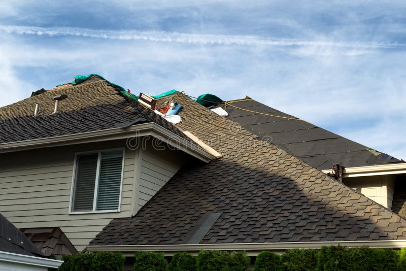 Home with roof being replaced showing new shingles, felt paper, and tools. Blue sky in background. Home with roof being replaced showing new shingles, felt paper, and tools. Blue sky in background.