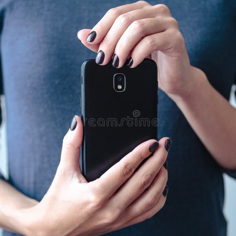 Black mobie smart phone in woman/s hands with perfect dark violet manicure over simple background. Black mobie smart phone in woman/s hands with perfect dark violet manicure over simple background