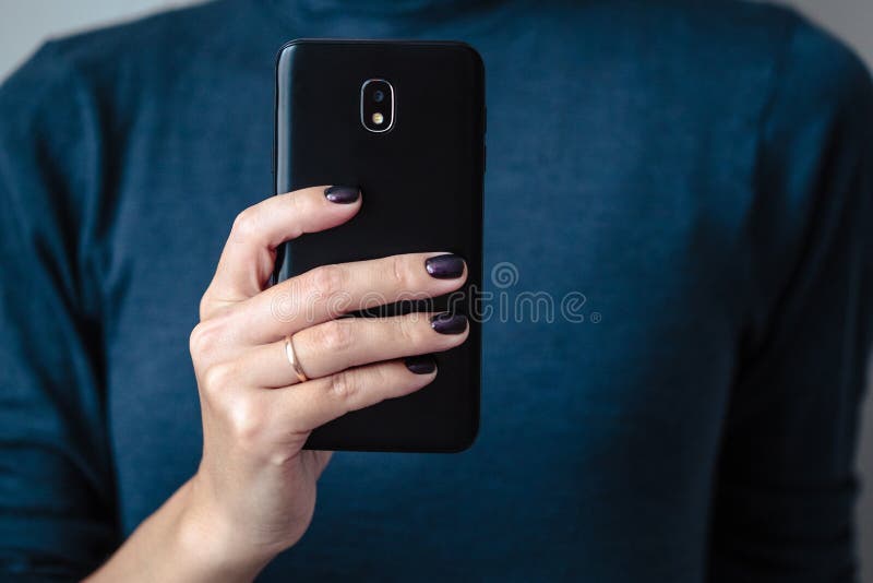 Black mobie smart phone in woman/s hands with perfect dark violet manicure over simple background. Black mobie smart phone in woman/s hands with perfect dark violet manicure over simple background