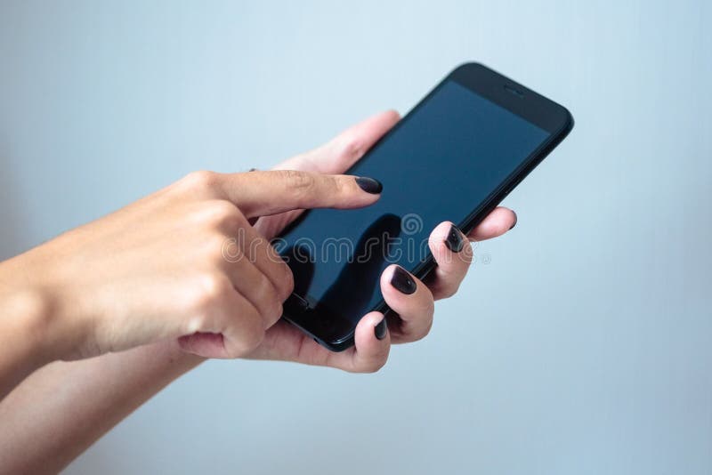 Black mobie smart phone in woman/s hands with perfect dark violet manicure over simple background. Black mobie smart phone in woman/s hands with perfect dark violet manicure over simple background